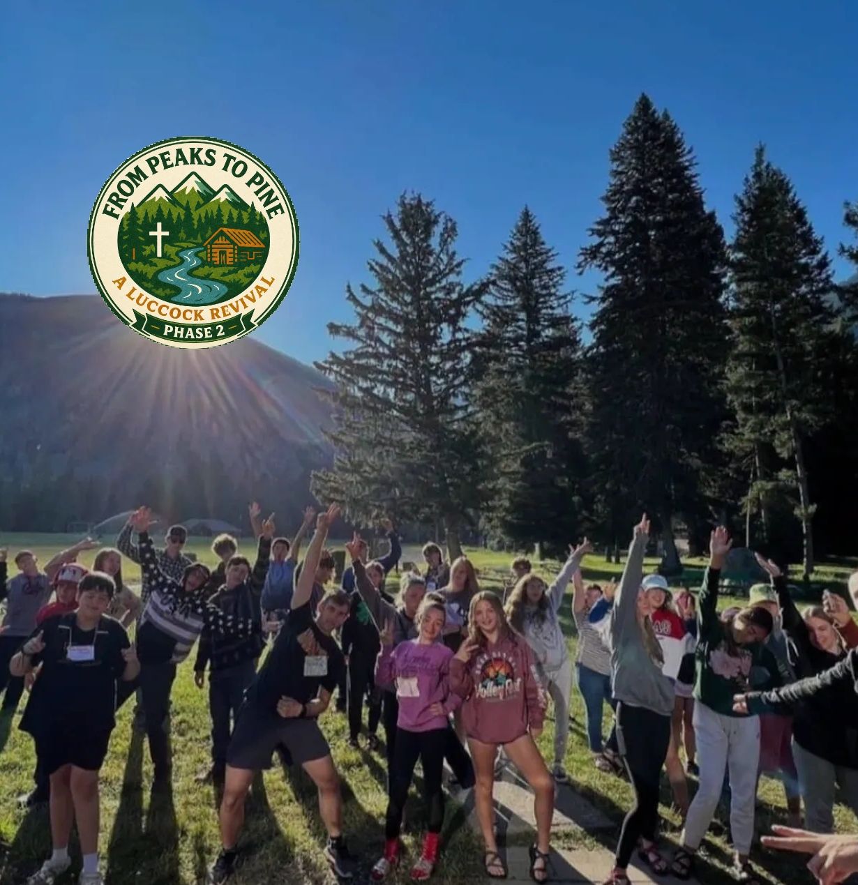A joyful group of young people outdoors with trees and mountains behind them.