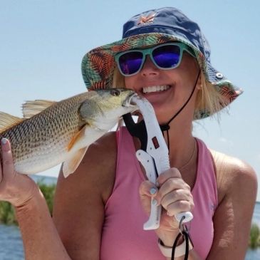 Smiling female fisherman holding a Red Drum fish with a fish gripper clamp
