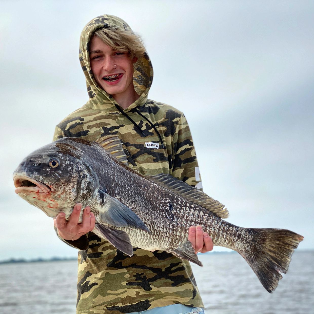 A teenage boy holding a large bull black drum in the beautiful Delacroix, Louisiana marsh.