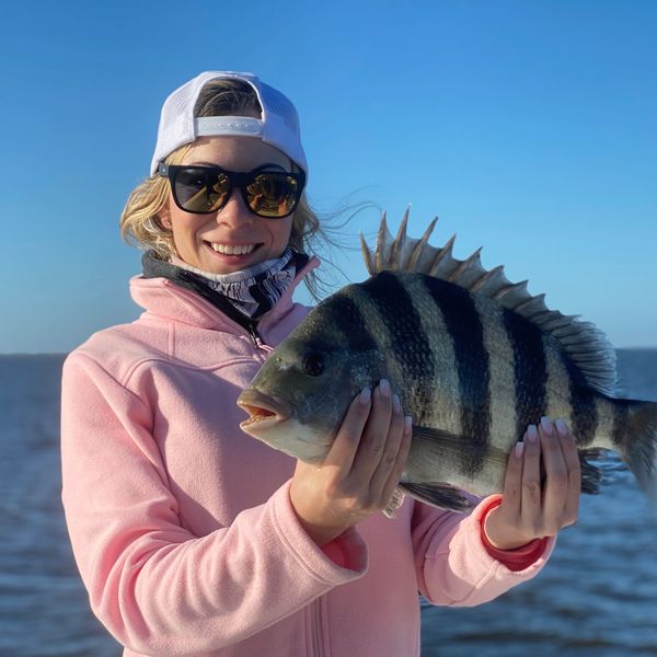 A woman holds a beautiful sheepshead fish with the marsh of Delacroix, Louisiana in the background.