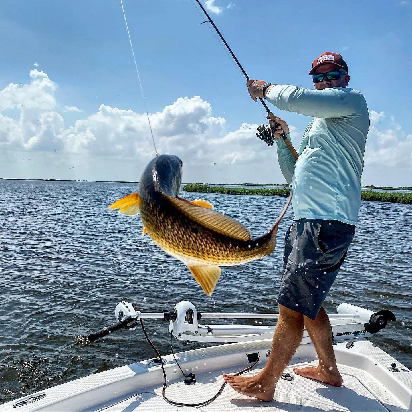 Male fisherman using the fishing rod to flip a red drum into the boat.