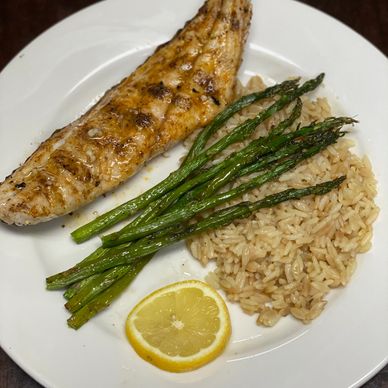 A plated meal of red drum (red fish) on the half shell with a bed of rice pilaf and asparagus