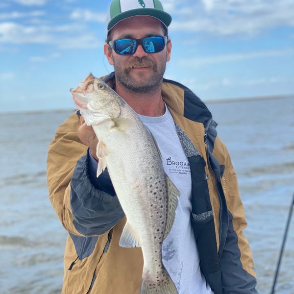 Man holding a nice keeper specked trout with the Delacroix, Louisiana marsh in the background.