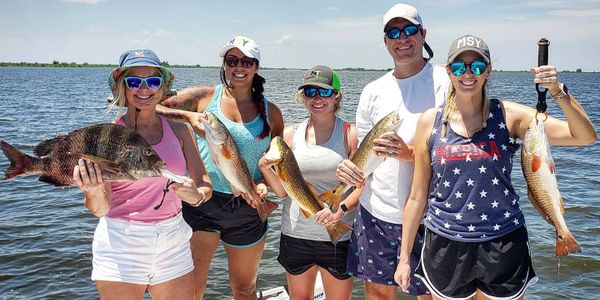 One make and four female fisherman smiling while holding red drum and sheepshead fish with the marsh
