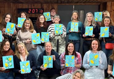 Group of women proudly displaying their flower paintings indoors.