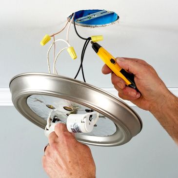 Hands installing a ceiling light fixture using a voltage tester.