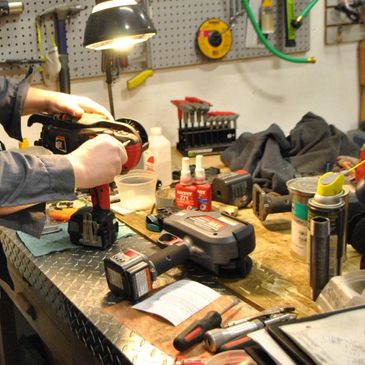 Person using a power tool on a workbench filled with various tools and supplies.