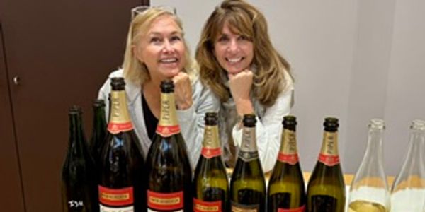 Two women smiling behind bottles of sparkling wine.