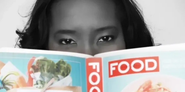 Person peeking over a colorful food magazine with intense eyes.