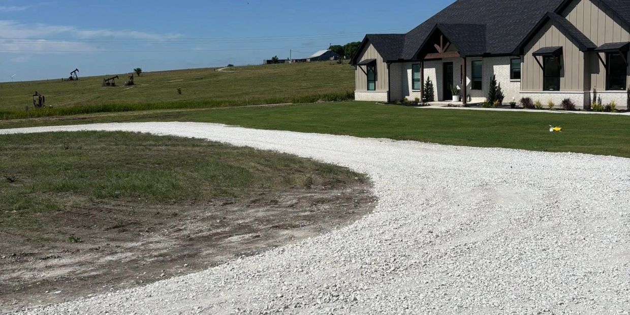 A modern beige house with a curved gravel driveway in a rural setting.