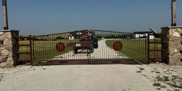 Gated gravel driveway with vehicles and rural house in background.