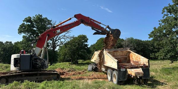 Excavator loading dirt into a dump truck in a field.