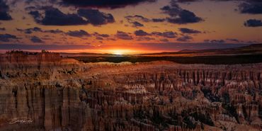 Sunset over a rugged canyon with layered rock formations and dramatic clouds.
