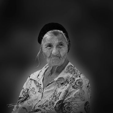 Black and white portrait of an elderly woman with a patterned shirt and beanie.
