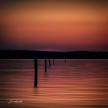 Sunset over calm water with silhouetted posts.
