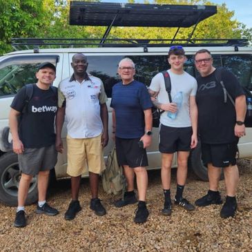 Group of five men standing outdoors in front of a white vehicle.