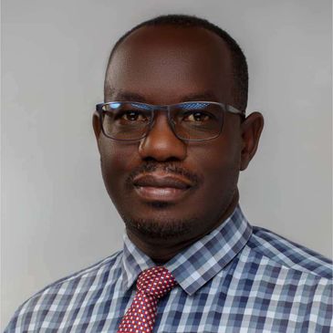 Portrait of a man wearing glasses, checkered shirt, and red tie.