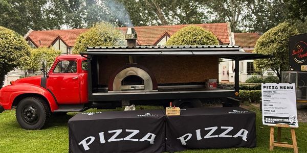 Mobile wood-fired pizza oven truck in a park.