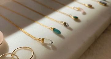 Close-up of delicate gold necklaces with various gemstone pendants displayed on a white surface.