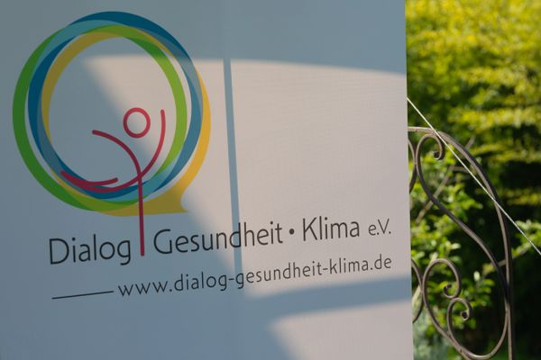 Signboard for Dialog Gesundheit Klima e.V. with colorful circular logo outdoors.