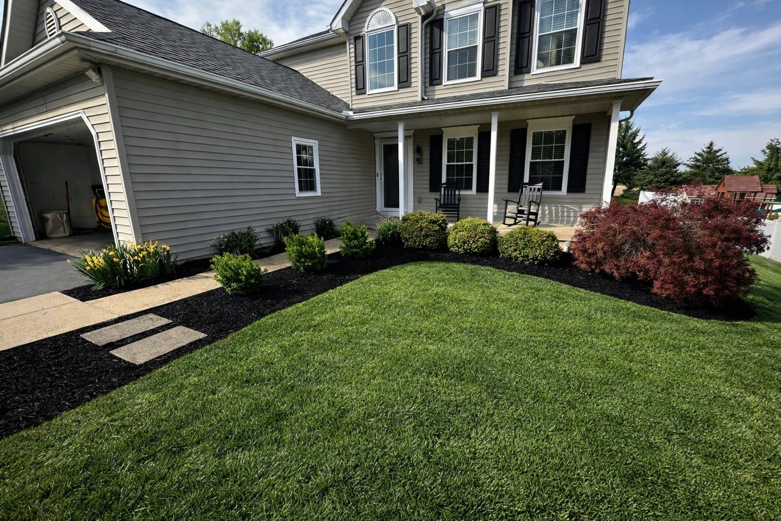 Well-maintained front yard with lush green grass, shrubs, and a welcoming porch with rocking chairs.