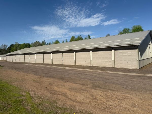 A row of closed beige garage doors under a blue sky with scattered clouds.