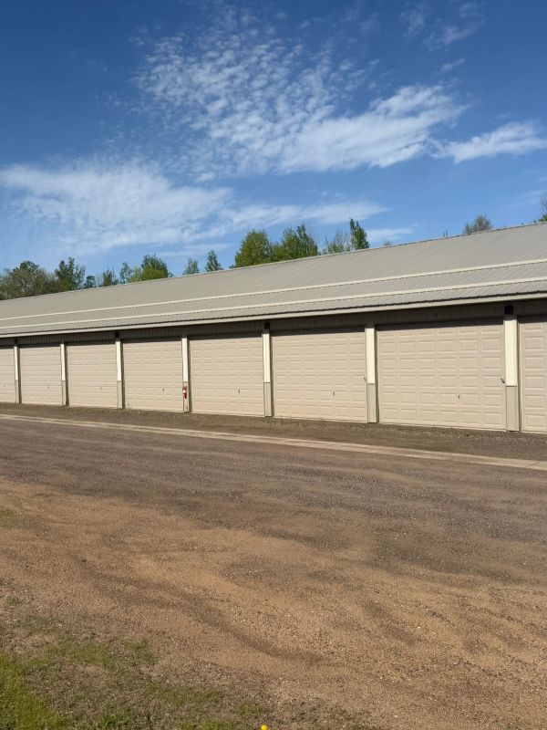 A row of closed beige garage doors under a blue sky with scattered clouds.