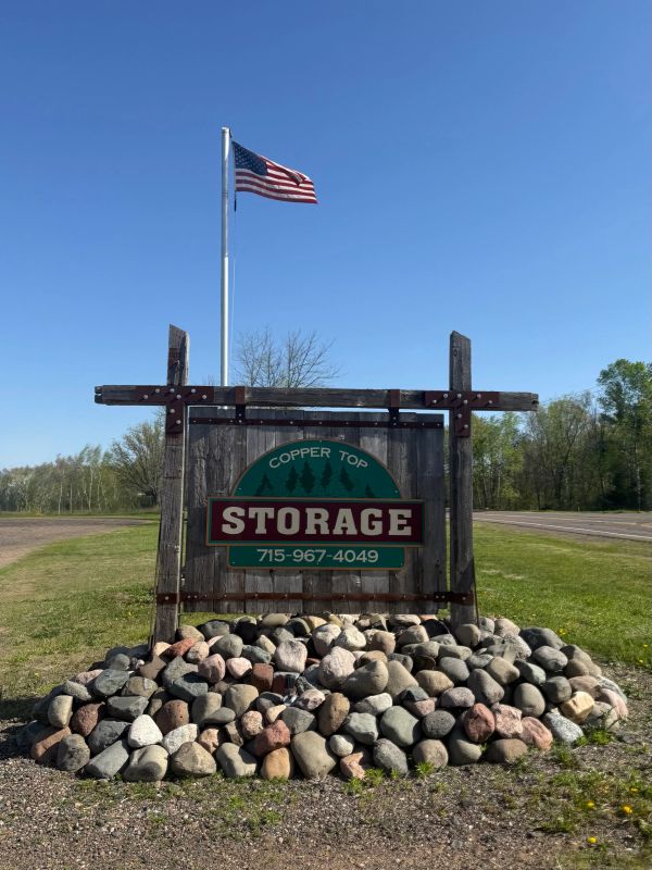 Rustic wooden sign for Copper Top Storage with American flag above.