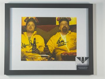 Framed signed photo of two men in yellow suits with headsets.