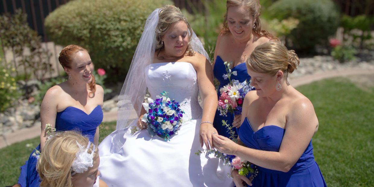 Bride surrounded by bridesmaids in blue dresses at outdoor wedding.