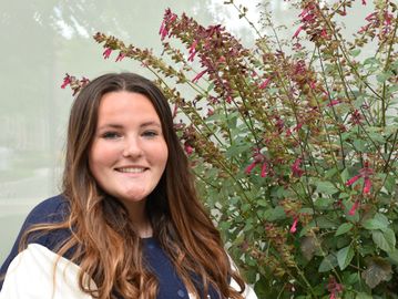 Senior portrait of a young woman wearing her senior jacket and flowers in the background