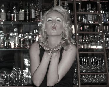 A woman blows kisses across the room while sitting on the counter of the bar at Scarlett's Lounge.