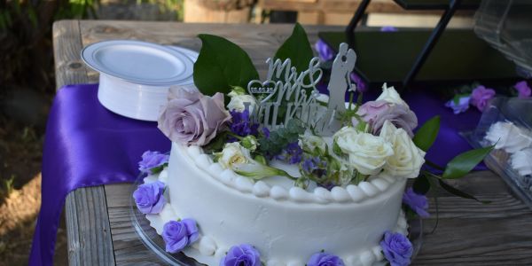 White wedding cake decorated with roses and purple flowers.