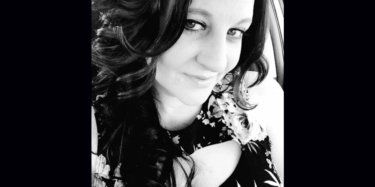 Woman with long dark hair smiling and wearing a floral dress.