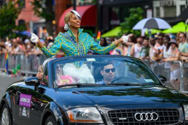 Person celebrating while standing in a convertible car during a parade.