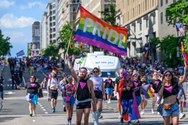 People marching with a large pride flag in a parade.