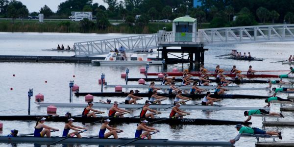 Teams rowing in a competitive race on calm water.