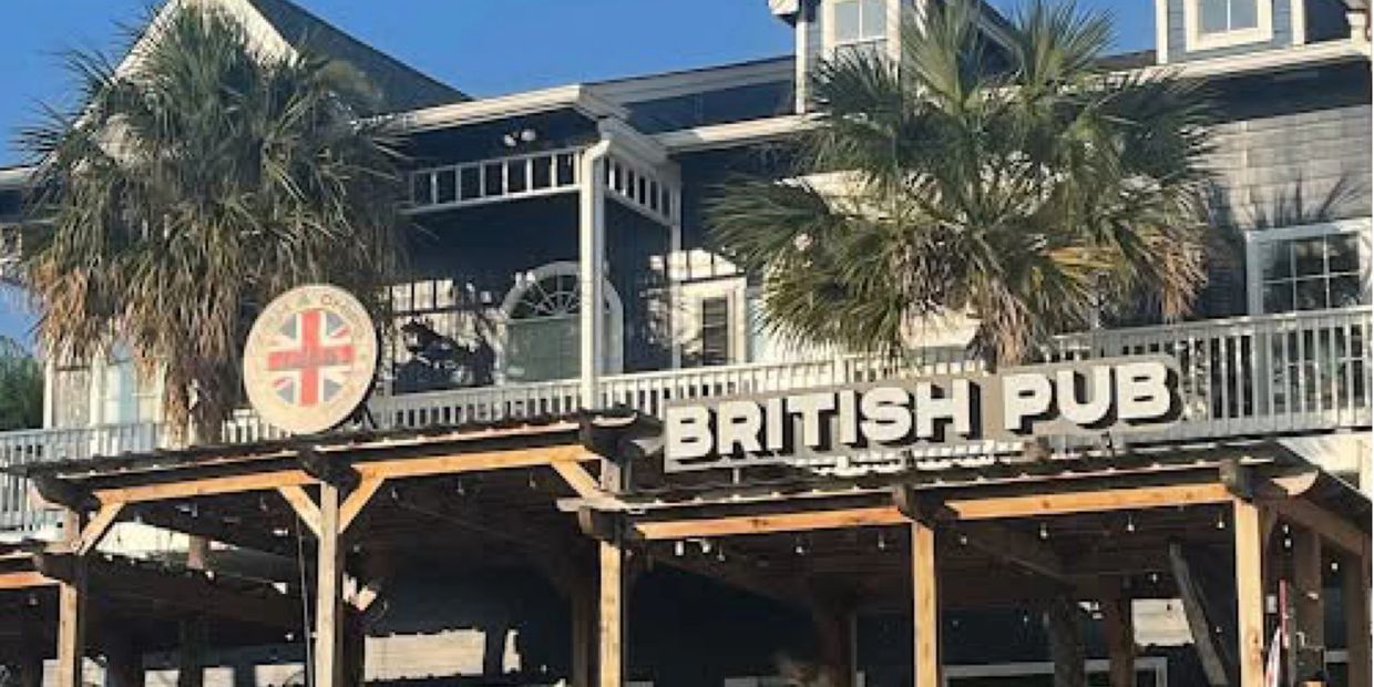 Exterior of a British pub with palm trees and wooden structure.