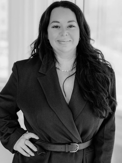 Confident woman in a belted blazer smiling warmly at the camera.