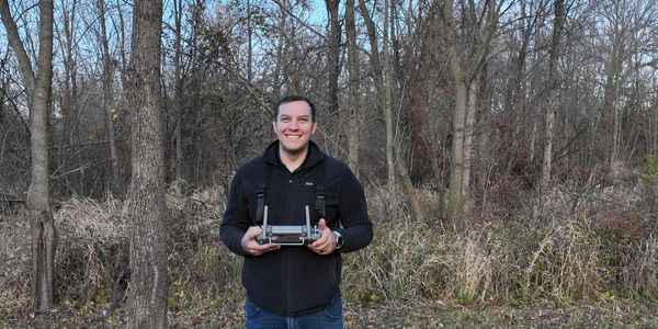Man holding a drone controller in a forest during fall.