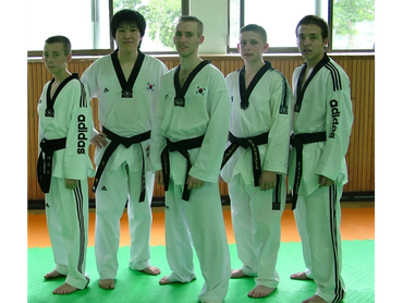Five taekwondo practitioners posing in uniform with black belts.
