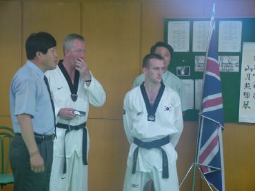 Group of men in martial arts uniforms near British flag indoors.