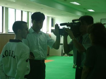 Man filming another man in an indoor green room.