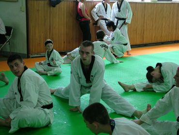 Group of people stretching in martial arts uniforms indoors.