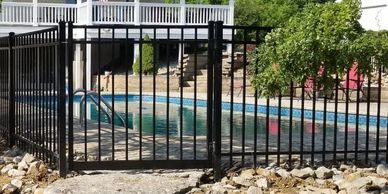 Rocky yard with a fenced pool and white house in the background.