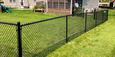 Black chain-link fence enclosing a green backyard with a playground and house.