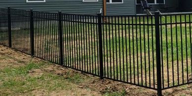Modern green house with a black metal fence around the yard on a sunny day.