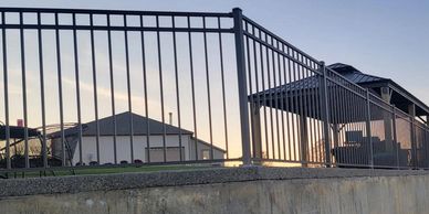 A fenced patio area on a raised concrete platform with green grass and trees in the background.