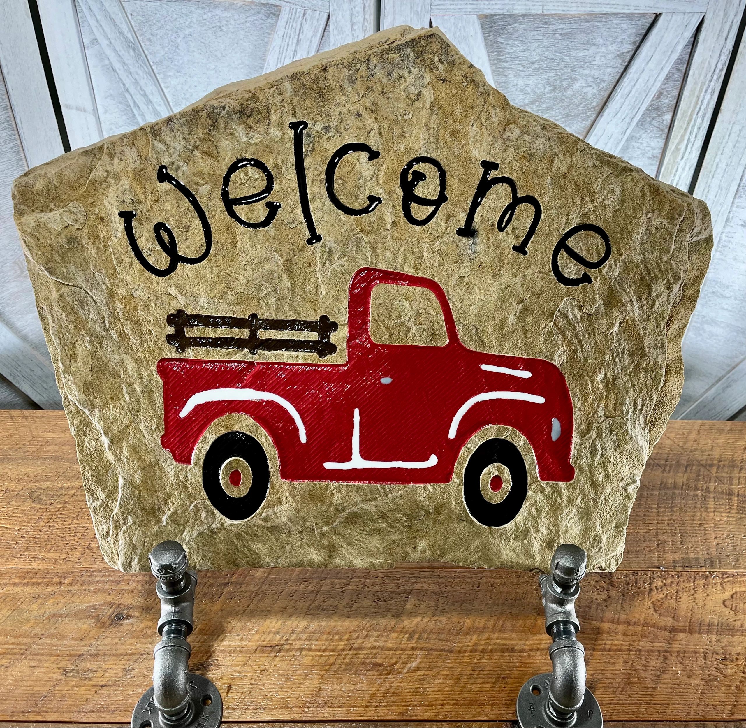Rustic welcome sign with a red truck painted on stone.
