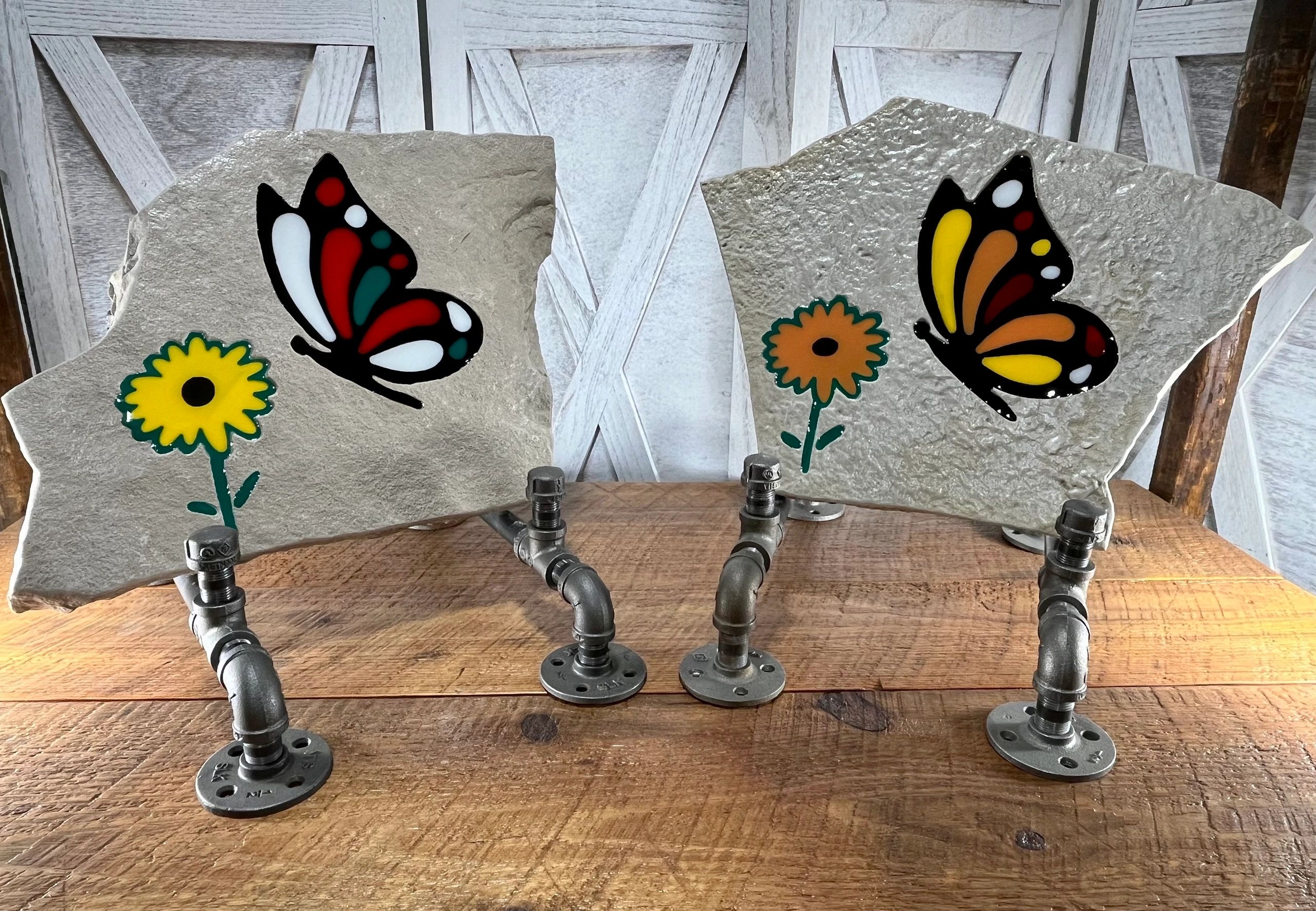 Two stone plaques with colorful butterfly and flower designs on metal stands.